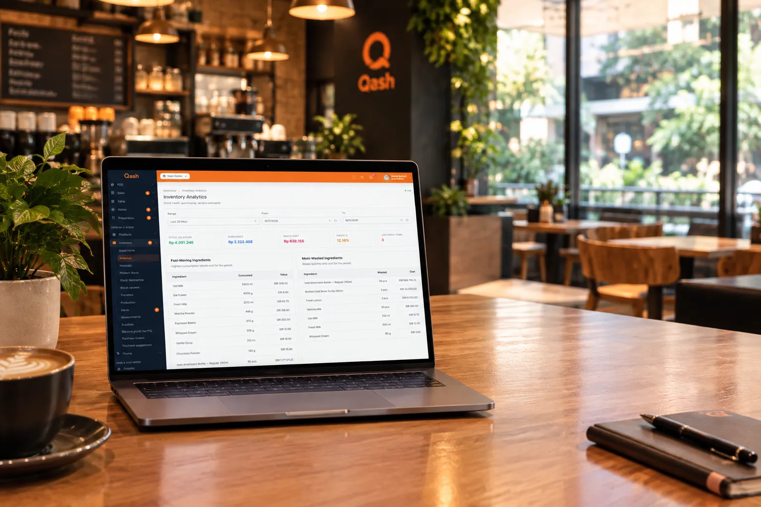 Laptop di meja kafe menampilkan analitik inventaris Qash, di samping secangkir kopi
