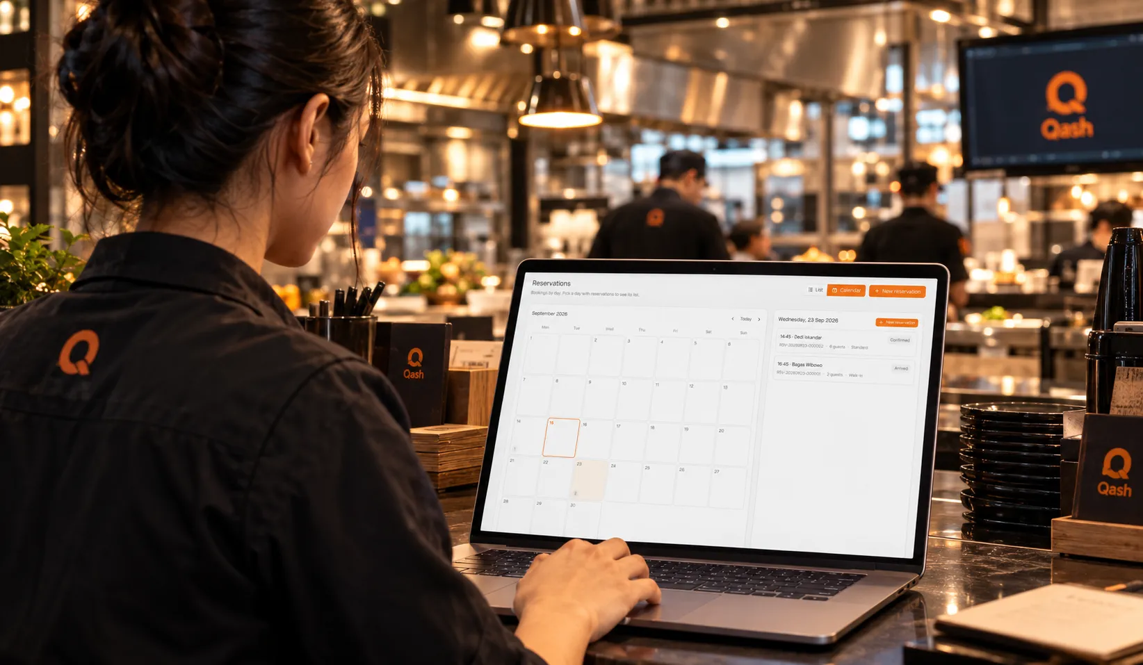Staf restoran di pass dapur membuka kalender reservasi Qash di laptop