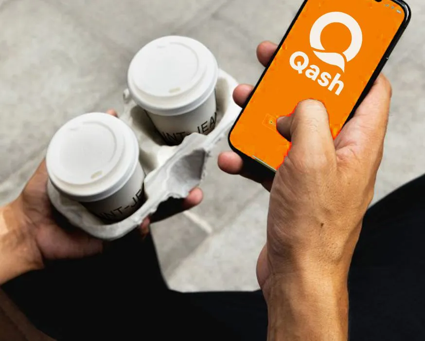 Tangan memegang dua kopi bawa pulang dan ponsel dengan aplikasi Qash