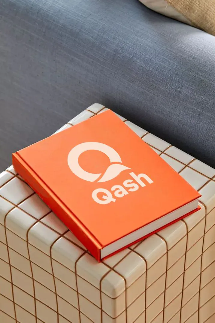 Buku oranye bersampul logo Qash di atas meja kecil berkeramik
