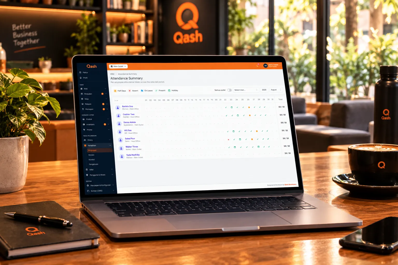 Laptop di meja kerja kafe menampilkan rekap kehadiran Qash, dengan logo Qash di dinding